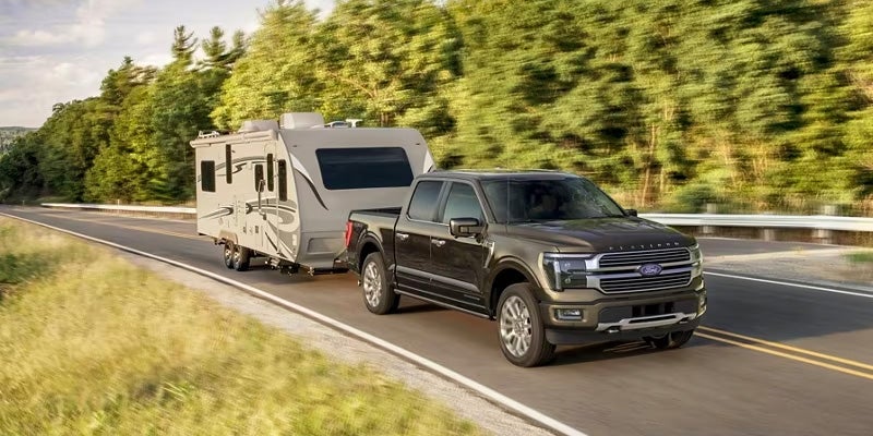 Ford F-150 pickup towing a large camper trailer on a scenic road.