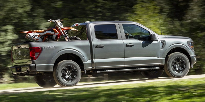 Ford F-150 FX4 truck carrying a dirt bike on a forest trail.