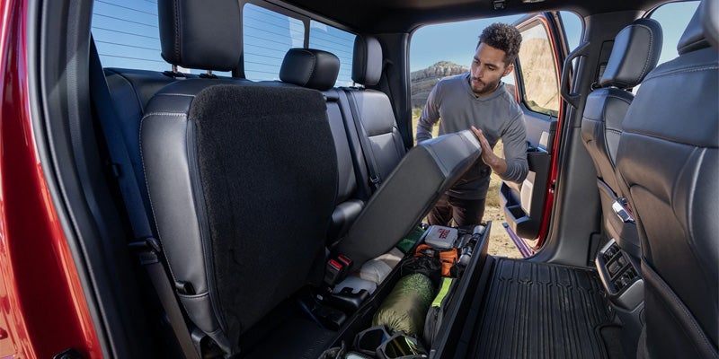Man organizing gear under rear seat storage in a Ford F-150 truck.
